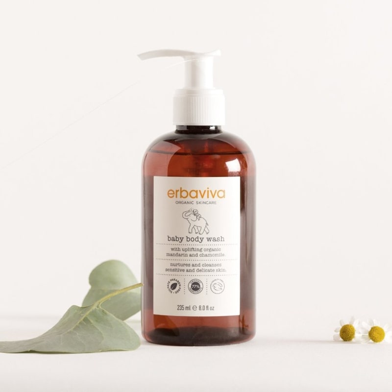 Lifestyle shot of Erbaviva Baby Body Wash (8 oz) with green leaves and small daisy flowers in the background