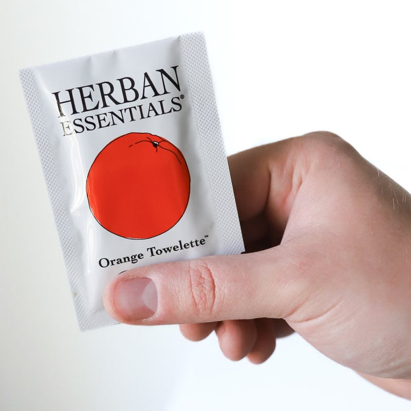 Herban Essentials single orange towelette shown in model's hand