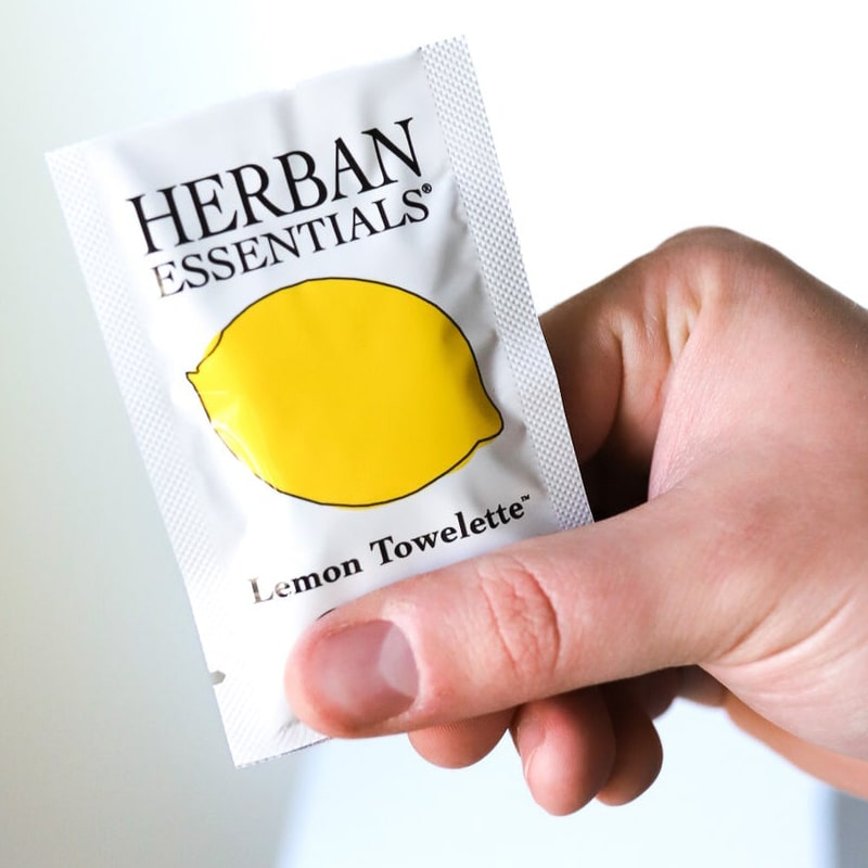 Herban Essentials single lemon towelette shown in model&#39;s hand