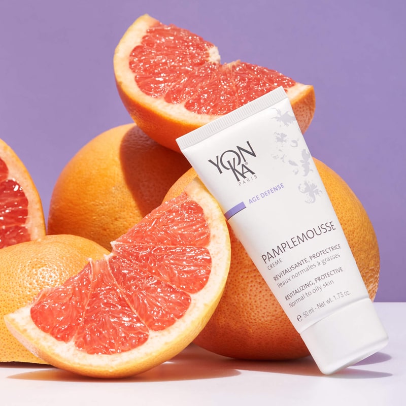 Lifestyle shot of Yon-Ka Paris Pamplemousse Creme PNG for Normal to Oily Skin (50 ml) with whole and sliced grapefruit in the background