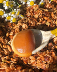 Activist Manuka Surfer's Honey 50+MGO shown on spoon to show color and texture with grains and flowers in the background