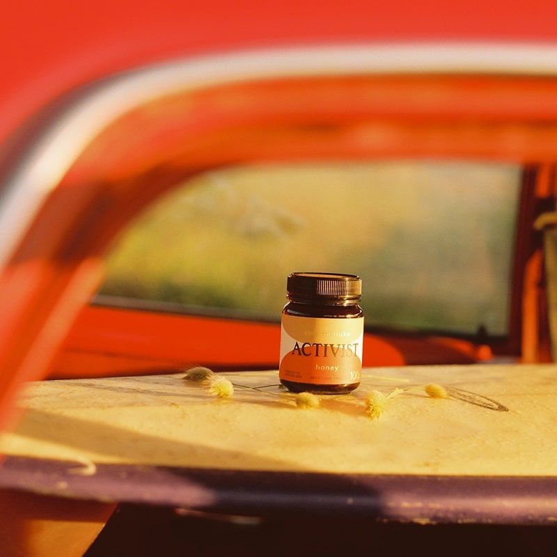 Lifestyle shot of Activist Manuka Surfer's Honey 50+MGO (12 oz) sitting on surfboard and care in the background