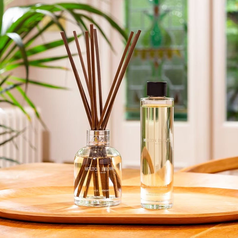 Lifestyle shot of Molton Brown Orange & Bergamot Aroma Reeds Diffuser (150 ml) shown next to bottle of refill (150 ml)