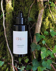 Lifestyle shot of ISUN Emerald Body Serum (100 ml) with mossy tree and ivy in the background