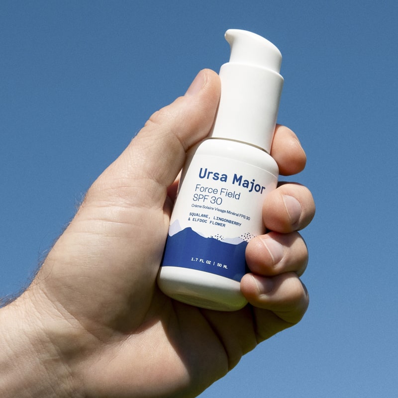 Lifestyle shot of Ursa Major Force Field SPF 30 shown in hand of model with blue sky in the background