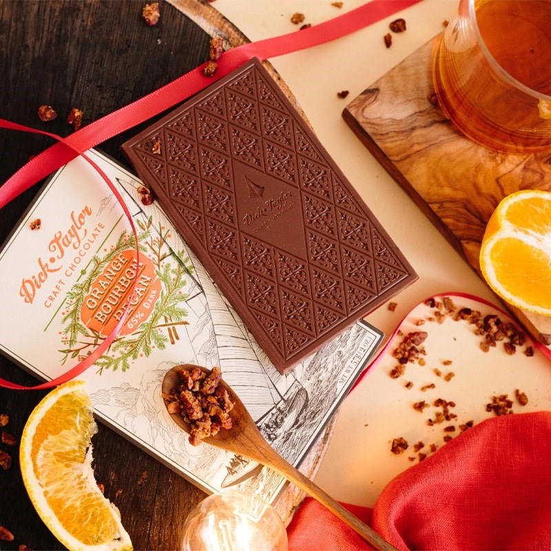 Dick Taylor Craft Chocolate Orange Bourbon Pecan Dark Chocolate - product shown next to ingredients and ribbon and wood block