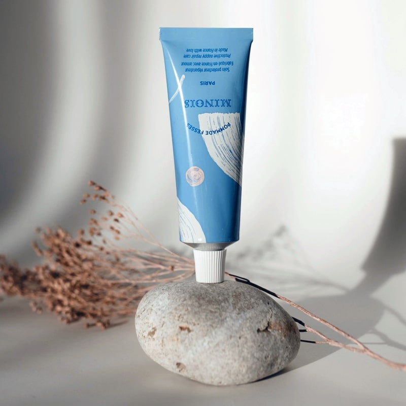 Lifestyle shot of Minois Paris Pommade Fesses (Diaper Cream) (50 ml) tube on rock with dried flowers in the background