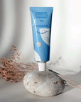 Lifestyle shot of Minois Paris Pommade Fesses (Diaper Cream) (50 ml) tube on rock with dried flowers in the background