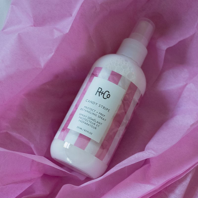 R+Co Candy Stripe Protect + Prep Detangling Spray - product shown in pink tissue paper