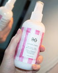 R+Co Candy Stripe Protect + Prep Detangling Spray - model holding product in front of mirror