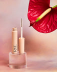 Lifestyle shot of Rye Beauty Brow Milk (6 ml) tube shown open with wand and red anthurium flower in the background