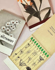 The Quiet Botanist In The Weeds Scented Candle - product matchbooks opened and closed shown