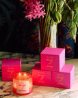 ROEN Candles De Las Flores Scented Candle - product shown lit next to boxes and flowers