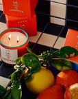 ROEN Candles La Condesa Scented Candle - product shown lit next to bowl of fruit and packaging