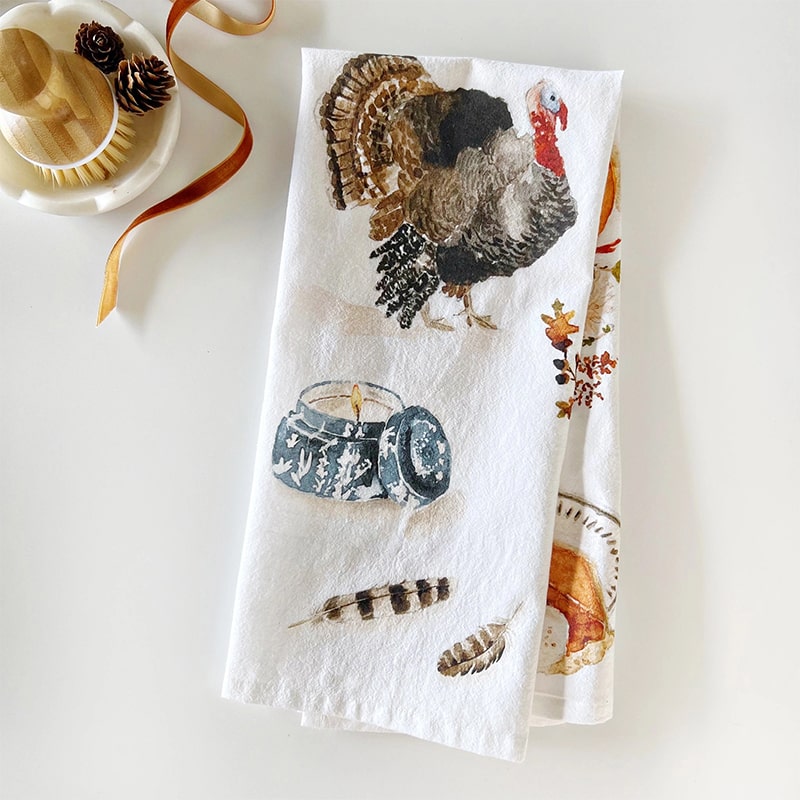 Emily Lex Studio Thanksgiving Tea Towel - product shown folded next to cleaning brush and ribbon