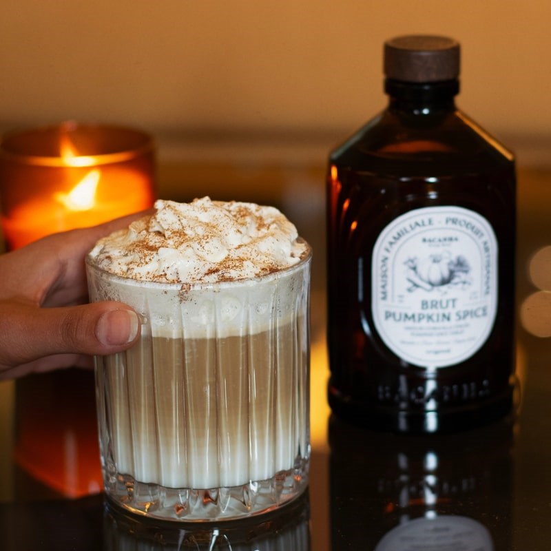 Lifestyle shot of drink with whipped cream next to bottle of Bacanha Organic Raw Pumpkin Spice Syrup (400 ml)