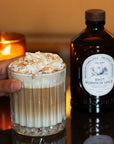 Lifestyle shot of drink with whipped cream next to bottle of Bacanha Organic Raw Pumpkin Spice Syrup (400 ml)