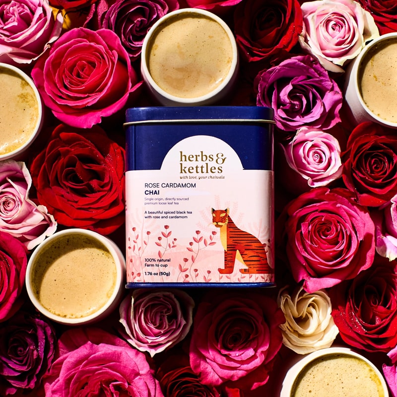 Herbs & Kettles Rose Cardamom Chai - product packaging shown on top of roses and cups of tea