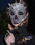 Model wearing crystal Halloween skull mask with face, neck and shoulder adorned with paper moths