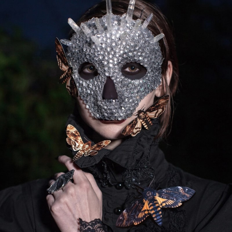 Model wearing crystal Halloween skull mask with face, neck and shoulder adorned with paper moths