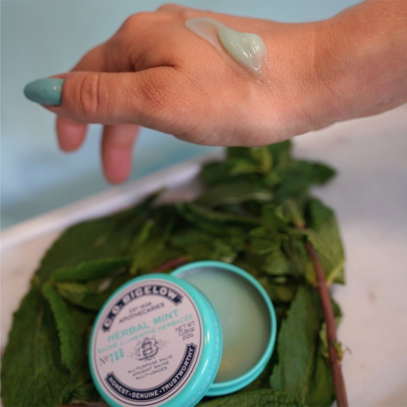 C.O. Bigelow Herbal Mint Salve Lip Tin - model with product smear on hand near opened product container