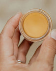 Smithereen Farm Bixa Fixa Healing Salve - model holding opened product showing texture and color