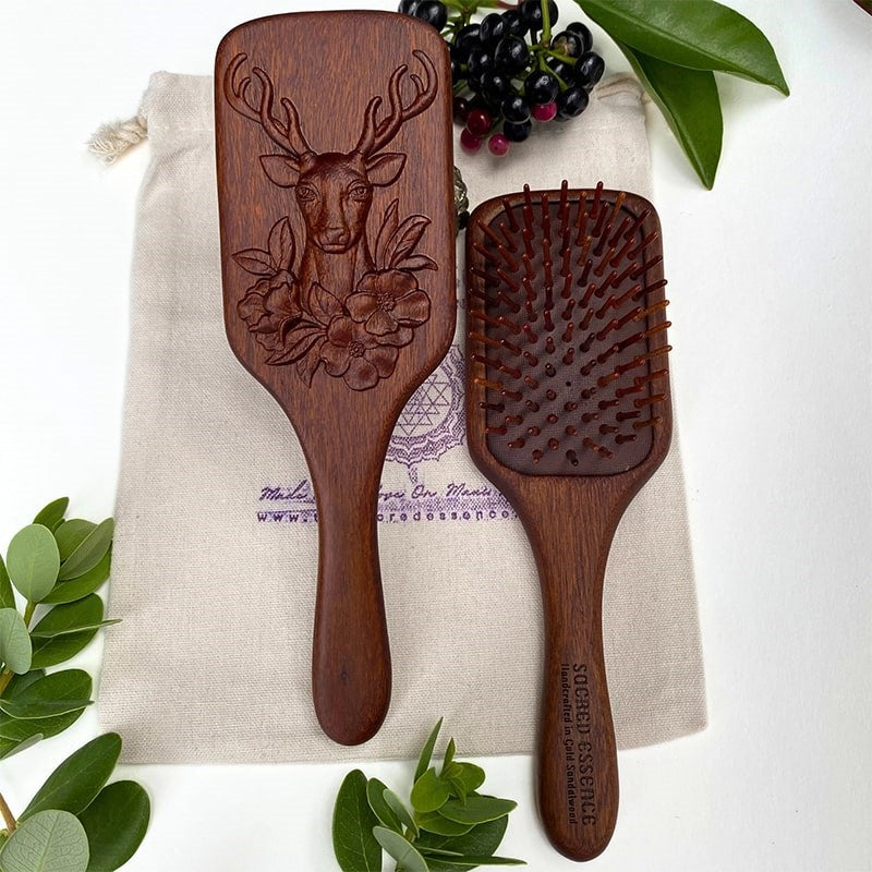 The Sacred Essence Deer Scalp Massage Brush in Golden Sandalwood - product shown next to plants non included bag