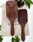 The Sacred Essence Deer Scalp Massage Brush in Golden Sandalwood - product shown next to plants non included bag