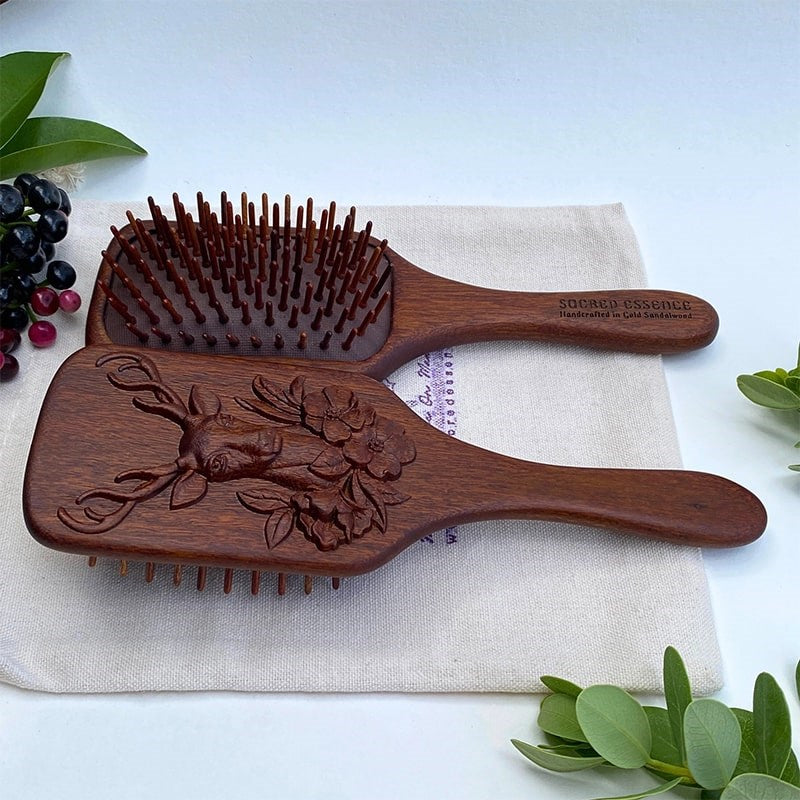 The Sacred Essence Deer Scalp Massage Brush in Golden Sandalwood - angled view of product next to plants