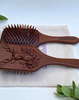 The Sacred Essence Deer Scalp Massage Brush in Golden Sandalwood - angled view of product next to plants