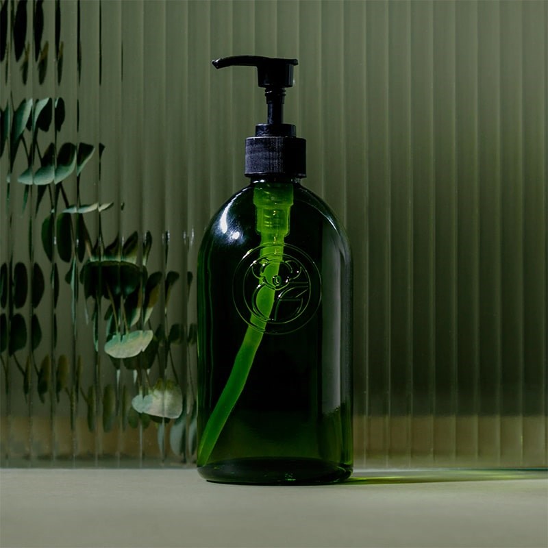 Koala Eco Apothecary Glass Bottle and Pump - product shown in front of glass and plant