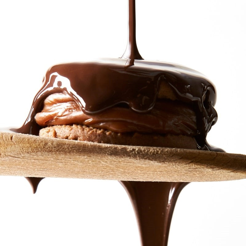 Wooden Table Baking Company Chocolate Covered Alfajores Cookies - product shown on wooden spoon with dripping chocolate 