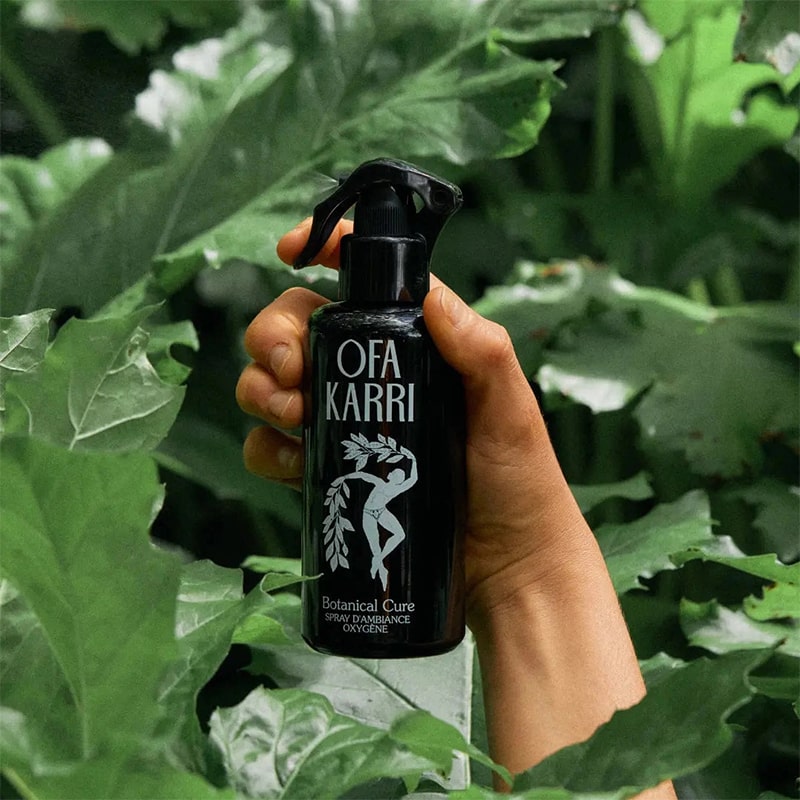 Lifestyle shot of model holding Ofa Karri Botanical Cure Home Spray (200 ml) with leaves in the foreground and background