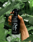 Lifestyle shot of model holding Ofa Karri Botanical Cure Home Spray (200 ml) with leaves in the foreground and background