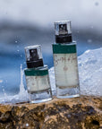 Lifestyle shot of Santos de Ibiza Facial Mist (100 ml and 50 ml) sitting on rock with ocean and waves crashing behind the rock