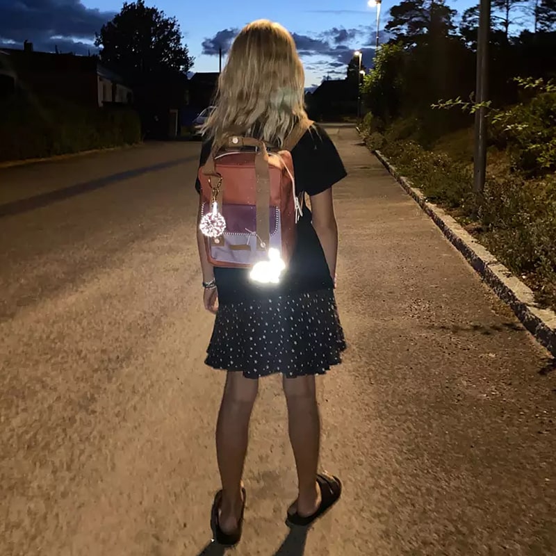 Firefly Reflectors Reflective Pom Pom - Rose shown on girl's backpack at night reflecting