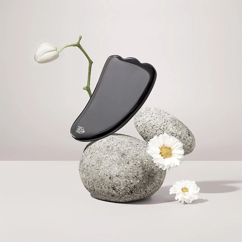 Snow Fox Skincare Black Obsidian Hot Stone Gua Sha - product shown on rocks with flowers