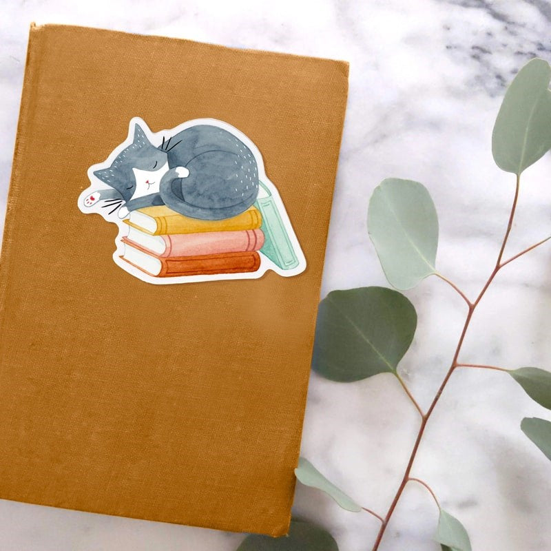 Julianna Swaney Cat and Books Sticker - product shown on top of book by branch