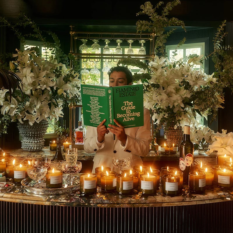 Flamingo Estate Organics The Guide to Becoming Alive - model shown holding product near lit candles and flowers